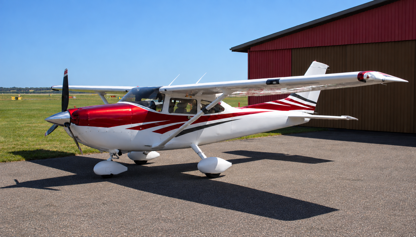 Single-engine Cessna with wing strut mounts parked on an apron in front of a hangar